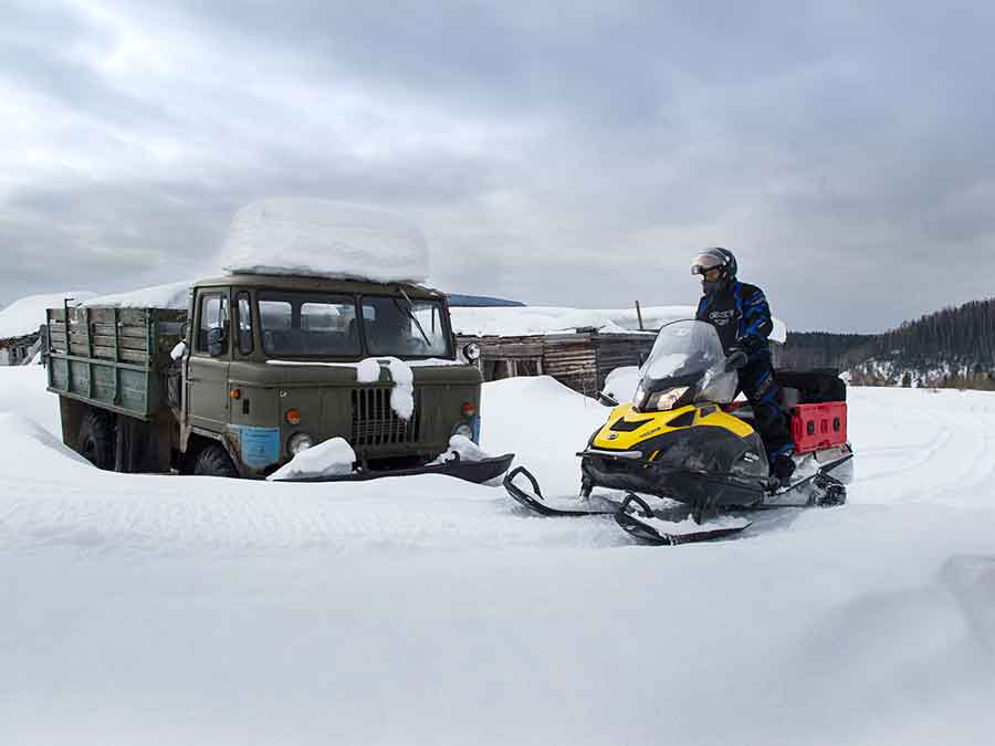 Igor Zapivalov snowmobiles by a Soviet era truck in abandoned village of Bolshaya