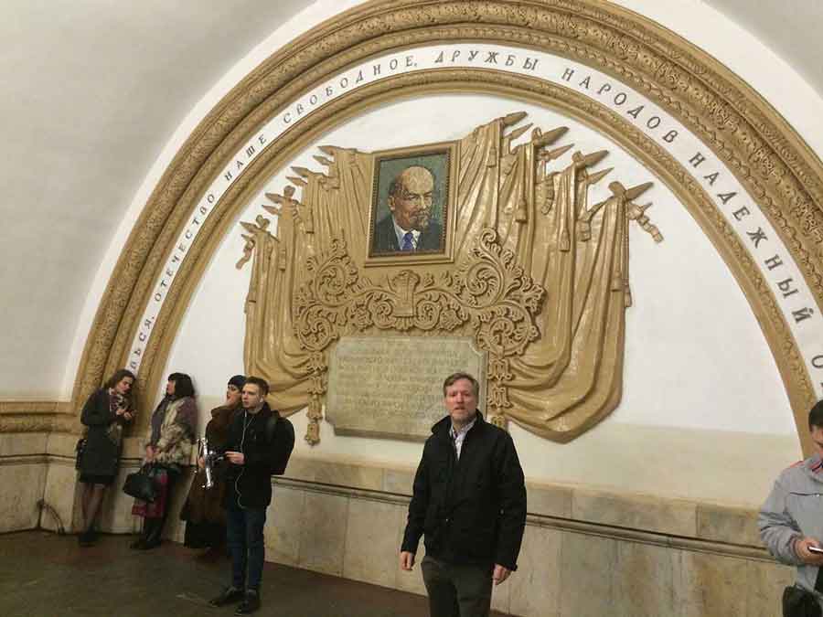 Dan Gould poses in Moscow subway in front of artwork from the former Soviet Union featuring Lenin.