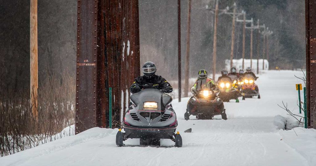 Snowmobiles cross railroad trestle in NH