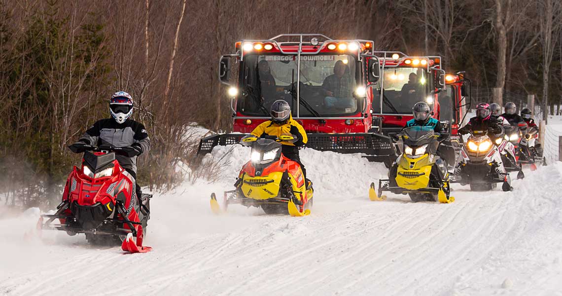 Snowmobiles passing a club trail groomer in Errol New Hampshire